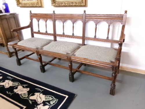 A late Victorian carved walnut three-seater bench featuring an arched spindle backrest, armrests, upholstered seat pads, and turned front legs. View V