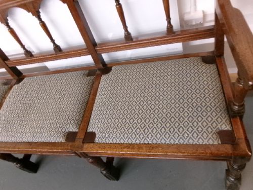 A late Victorian carved walnut three-seater bench featuring an arched spindle backrest, armrests, upholstered seat pads, and turned front legs. View VII