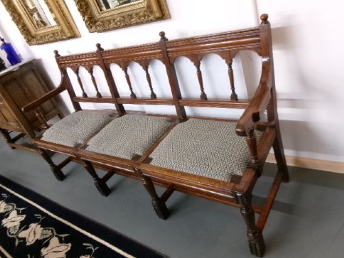 A late Victorian carved walnut three-seater bench featuring an arched spindle backrest, armrests, upholstered seat pads, and turned front legs. View IX