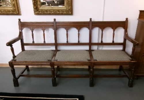 A late Victorian carved walnut three-seater bench featuring an arched spindle backrest, armrests, upholstered seat pads, and turned front legs. View X