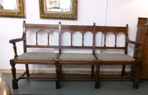 A late Victorian carved walnut three-seater bench featuring an arched spindle backrest, armrests, upholstered seat pads, and turned front legs. View XI