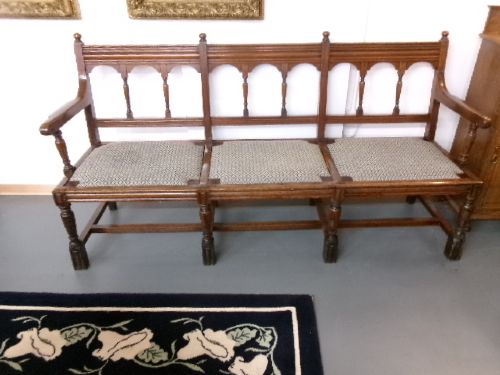 A late Victorian carved walnut three-seater bench featuring an arched spindle backrest, armrests, upholstered seat pads, and turned front legs. View XII