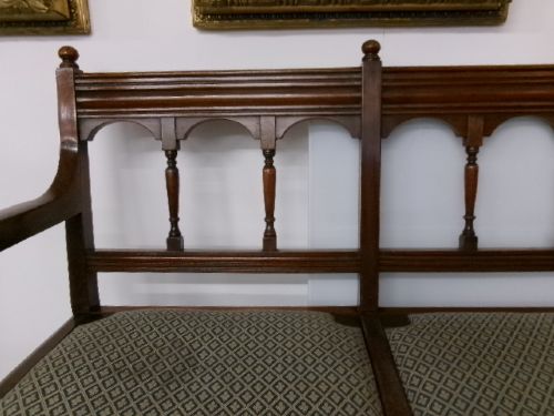 A late Victorian carved walnut three-seater bench featuring an arched spindle backrest, armrests, upholstered seat pads, and turned front legs. View XIII