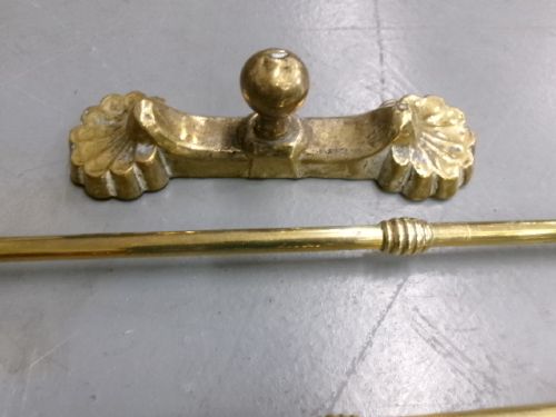 A brass fire companion set featuring two baluster-turned fire dogs, an iron rest, a pierced shovel, a poker, and tongs laid out on a surface. View VI