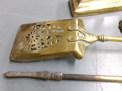 A brass fire companion set featuring two baluster-turned fire dogs, an iron rest, a pierced shovel, a poker, and tongs laid out on a surface. View VIII