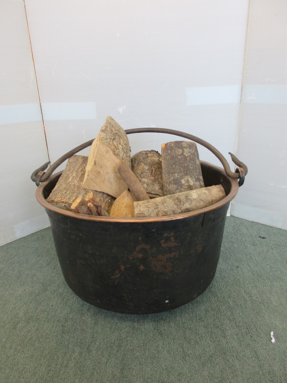 A dark patinated copper log bucket with an arched iron swing handle, filled with split logs.