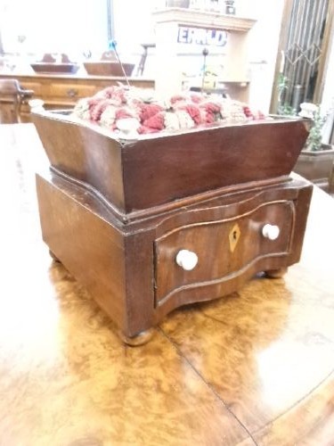 A 19th-century square mahogany pincushion featuring a padded fabric top above a small wooden drawer with two white knobs and bun feet.