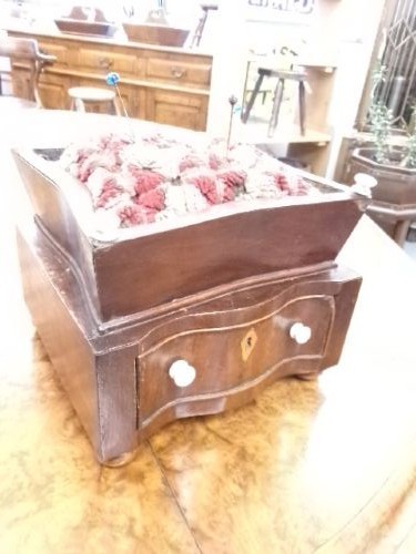 A 19th-century square mahogany pincushion featuring a padded fabric top above a small wooden drawer with two white knobs and bun feet. View II
