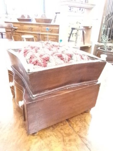 A 19th-century square mahogany pincushion featuring a padded fabric top above a small wooden drawer with two white knobs and bun feet. View V