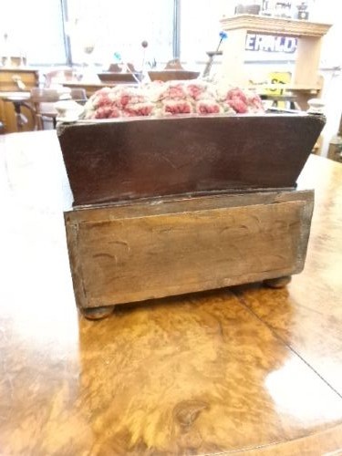 A 19th-century square mahogany pincushion featuring a padded fabric top above a small wooden drawer with two white knobs and bun feet. View VI