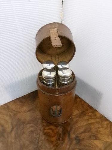A cylindrical tan leather case opened to reveal four glass flasks fitted with polished silver domed caps. View XII