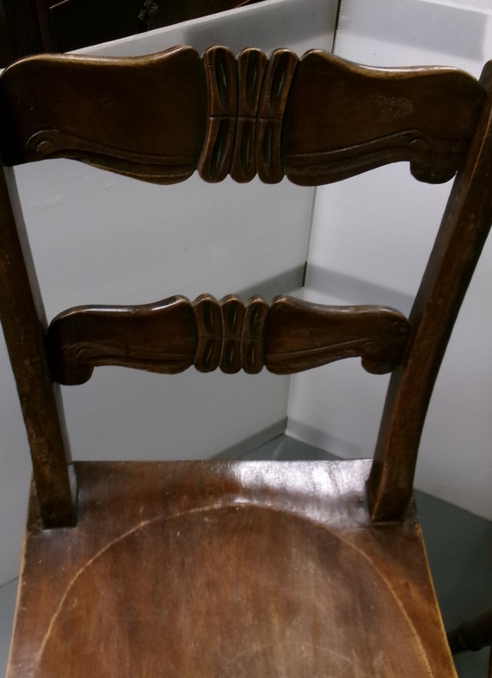 A pair of late Victorian dark brown wooden kitchen chairs with carved back rails, saddled wooden seats, and turned front legs. View II