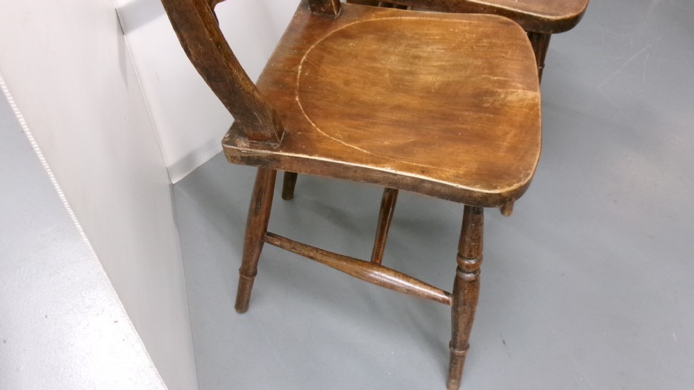 A pair of late Victorian dark brown wooden kitchen chairs with carved back rails, saddled wooden seats, and turned front legs. View IV