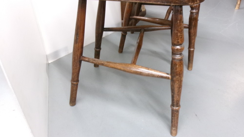 A pair of late Victorian dark brown wooden kitchen chairs with carved back rails, saddled wooden seats, and turned front legs. View V