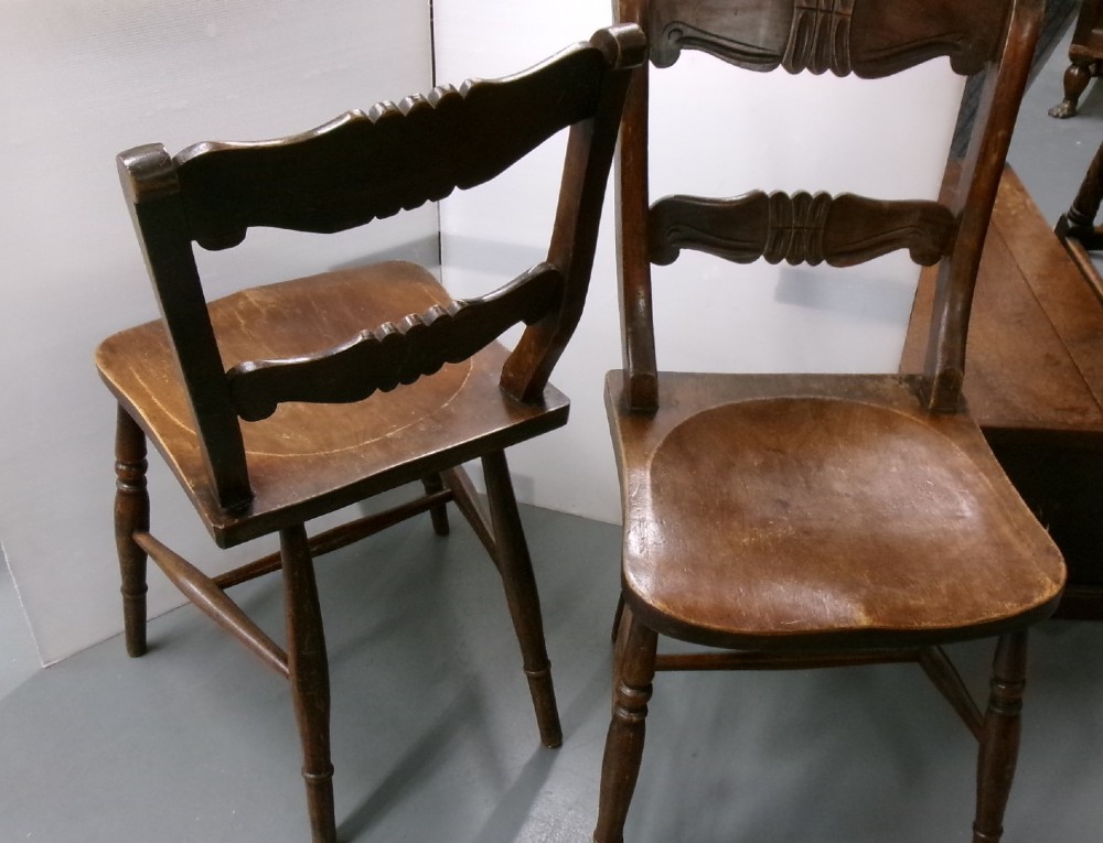 A pair of late Victorian dark brown wooden kitchen chairs with carved back rails, saddled wooden seats, and turned front legs. View VI