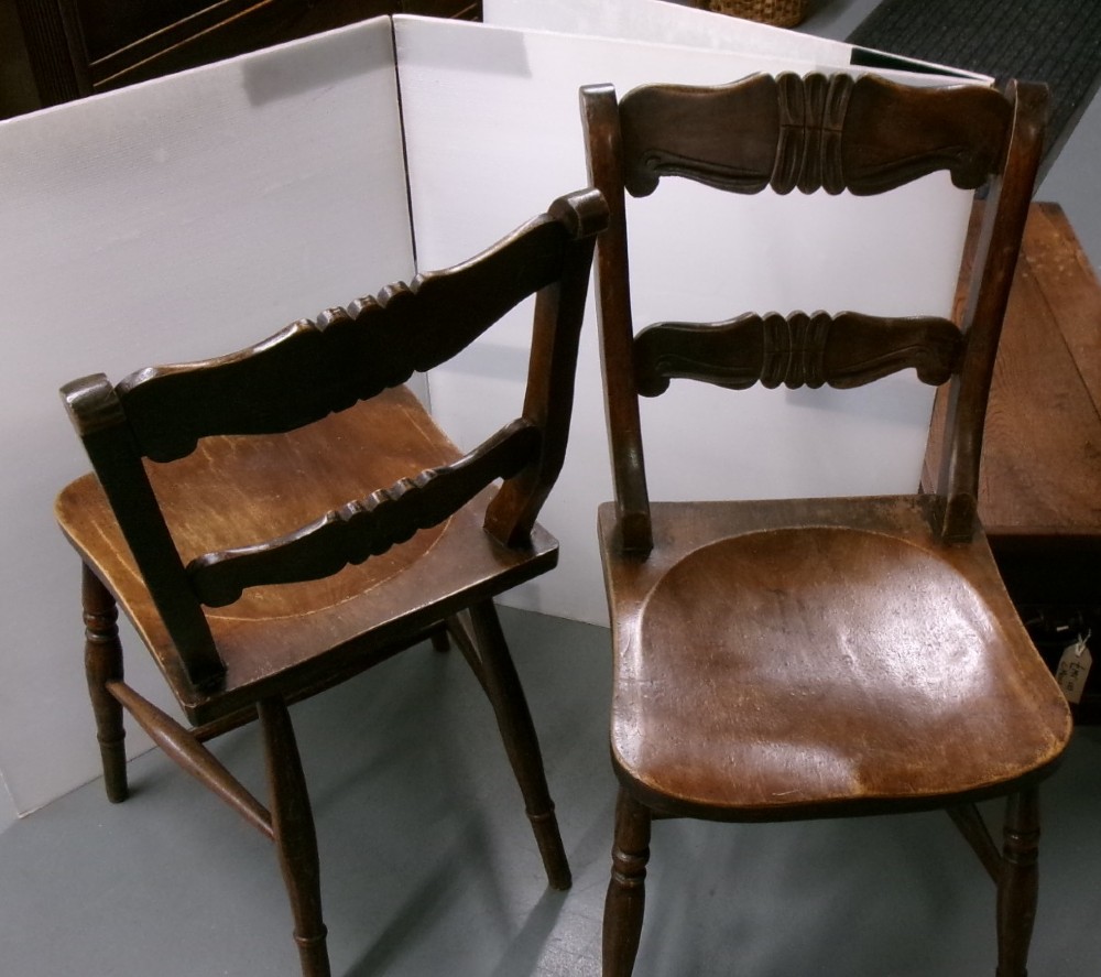 A pair of late Victorian dark brown wooden kitchen chairs with carved back rails, saddled wooden seats, and turned front legs. View VII