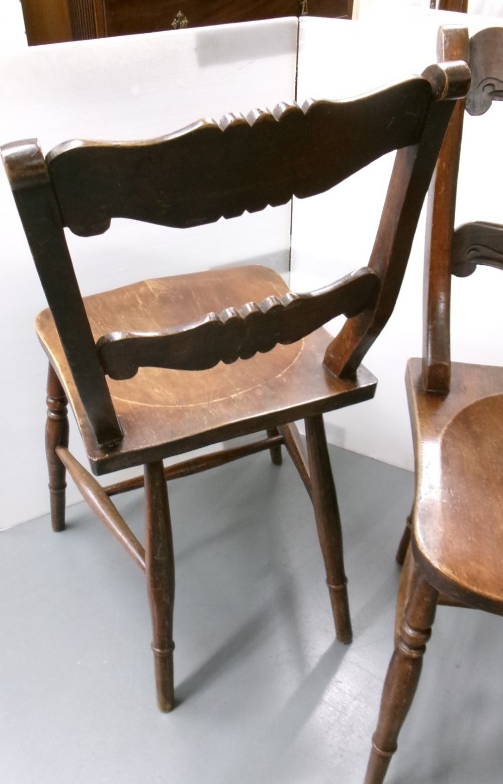 A pair of late Victorian dark brown wooden kitchen chairs with carved back rails, saddled wooden seats, and turned front legs. View VIII