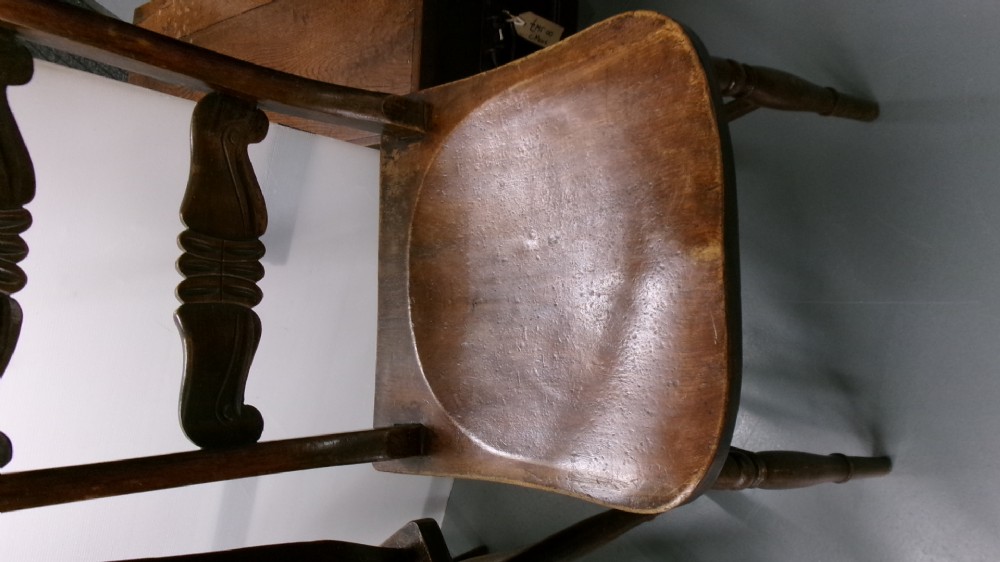 A pair of late Victorian dark brown wooden kitchen chairs with carved back rails, saddled wooden seats, and turned front legs. View IX