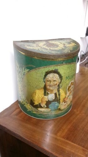 An antique semi-circular green tinplate tea caddy featuring a lithographed illustration of a woman drinking tea within an oval frame.