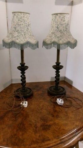 A pair of dark wood table lamps featuring carved barley twist stems, circular bases, and patterned fabric shades with fringed trim.