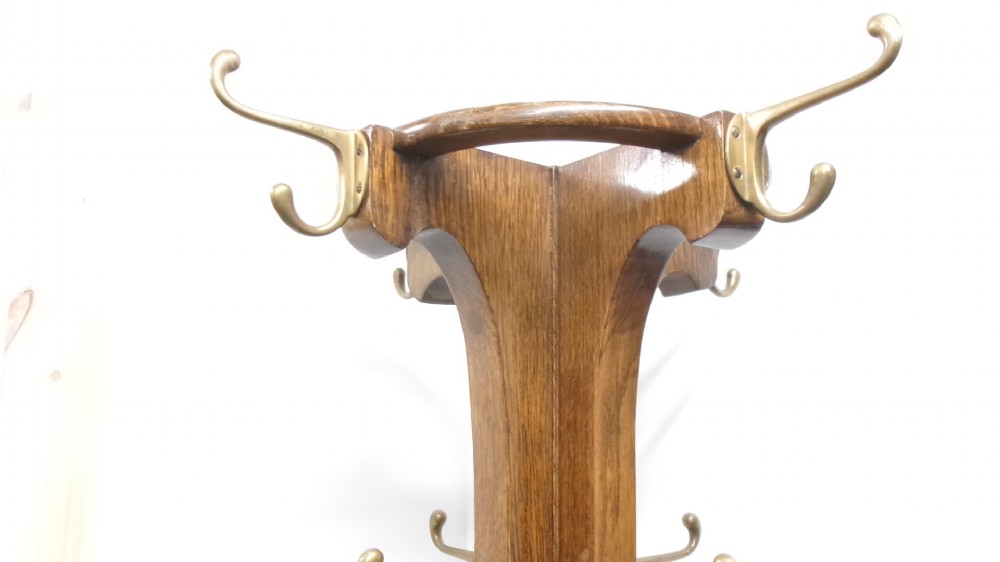 A tall solid oak hat and coat stand featuring multiple brass hooks, a tapered central column, and an integrated circular umbrella holder base. View VI