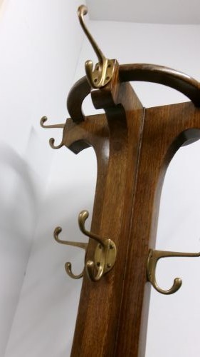 A tall solid oak hat and coat stand featuring multiple brass hooks, a tapered central column, and an integrated circular umbrella holder base. View IV