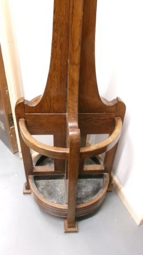 A tall solid oak hat and coat stand featuring multiple brass hooks, a tapered central column, and an integrated circular umbrella holder base. View II