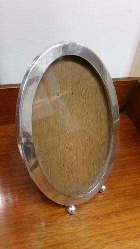 An oval sterling silver photo frame with a plain border, two ball feet, and a wooden backing. View II