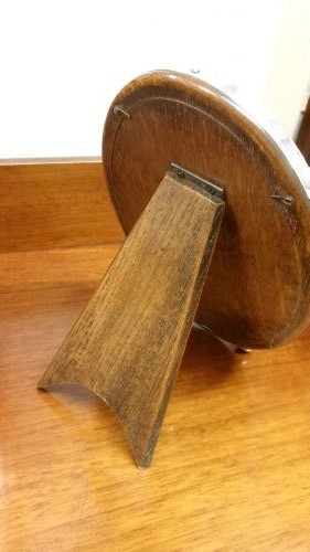 An oval sterling silver photo frame with a plain border, two ball feet, and a wooden backing. View III