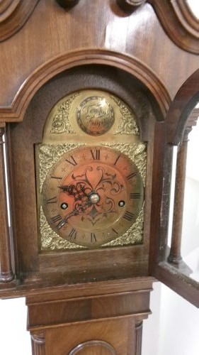 A slim mahogany granddaughter clock featuring a swan neck pediment hood, brass dial with spandrels, and an arched trunk door. View II