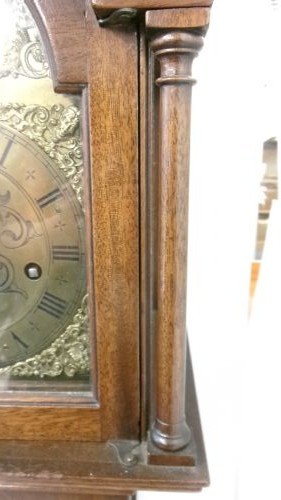 A slim mahogany granddaughter clock featuring a swan neck pediment hood, brass dial with spandrels, and an arched trunk door. View VII