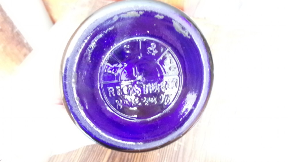 A tall Victorian cobalt blue glass apothecary bottle featuring a dark glass lollipop stopper and a gilt-bordered shield label inscribed SYR VIOLAE. View VII