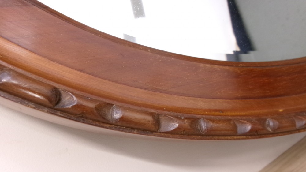 An Edwardian oval wall mirror crafted from mahogany timber featuring a carved decorative outer rim and bevelled glass. View II