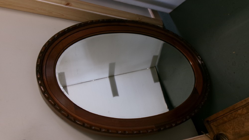 An Edwardian oval wall mirror crafted from mahogany timber featuring a carved decorative outer rim and bevelled glass. View III