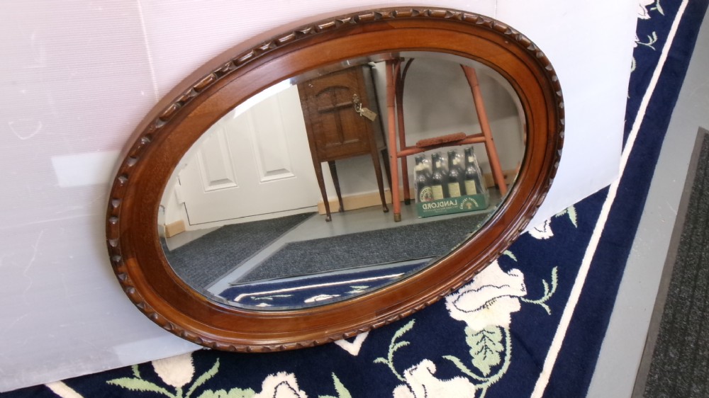 An Edwardian oval wall mirror crafted from mahogany timber featuring a carved decorative outer rim and bevelled glass. View VII