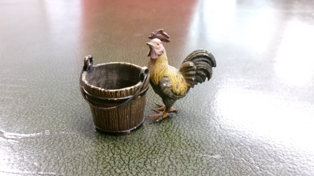 A small cold-painted bronze figurine depicting a cockerel standing alongside a miniature metal bucket with a handle. View II