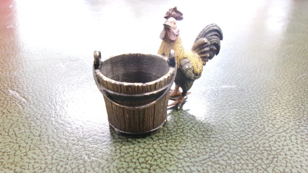 A small cold-painted bronze figurine depicting a cockerel standing alongside a miniature metal bucket with a handle. View III