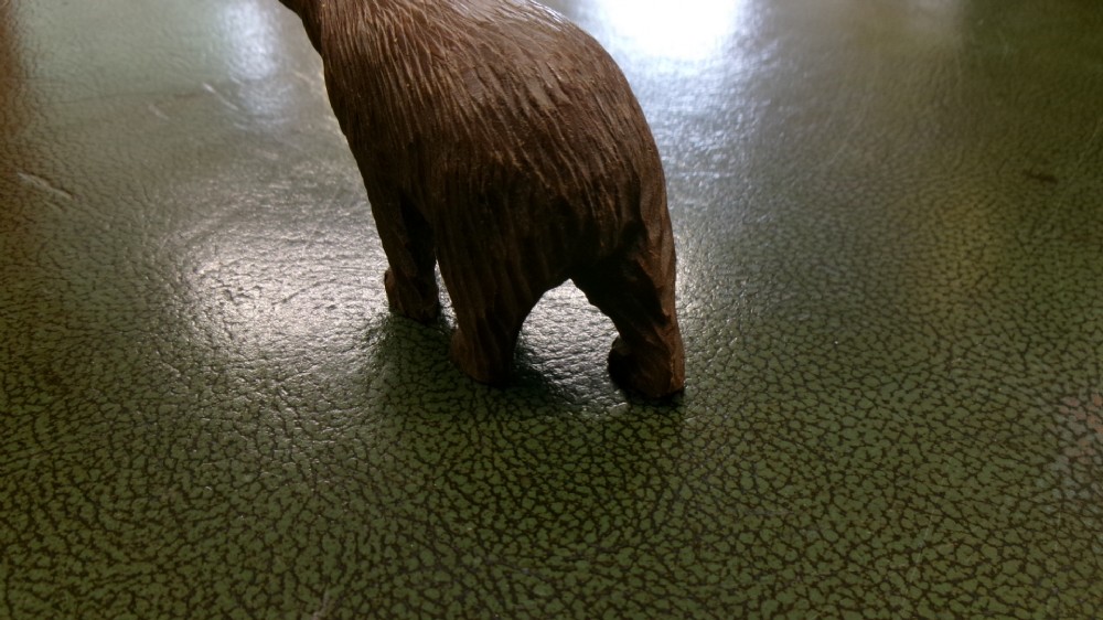 A hand-carved brown wooden bear figurine featuring textured fur, stud eyes, and an open painted red mouth. View V