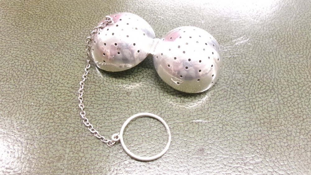 A spherical sterling silver tea infuser featuring fine round perforations, a hinged opening, and a chain attached to a finger ring. View IV