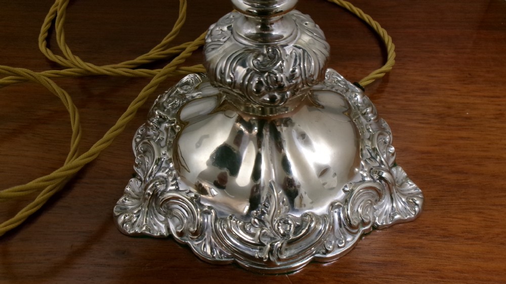 An Edwardian silver-plated table lamp base featuring Rococo scrollwork, a shaped baluster stem, and a moulded plinth base. View IV