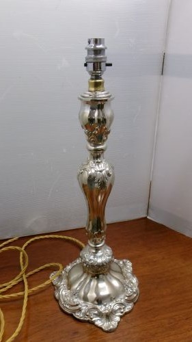 An Edwardian silver-plated table lamp base featuring Rococo scrollwork, a shaped baluster stem, and a moulded plinth base.