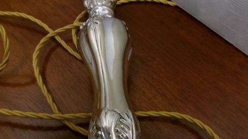 An Edwardian silver-plated table lamp base featuring Rococo scrollwork, a shaped baluster stem, and a moulded plinth base. View IX