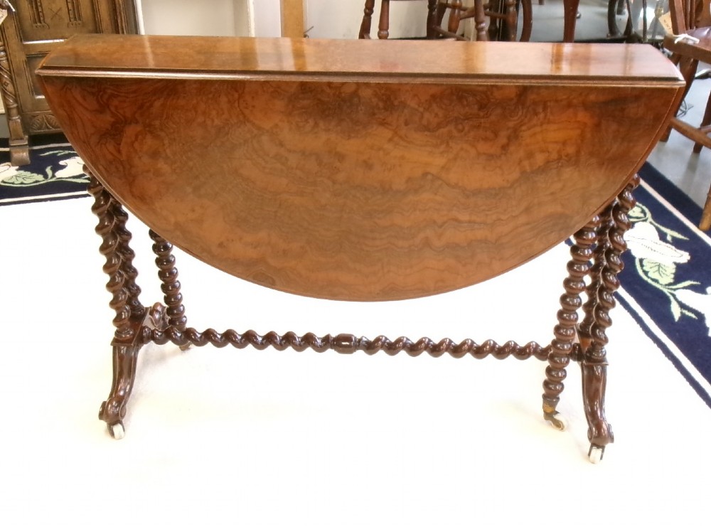 A Victorian burr walnut Sutherland table featuring hinged drop leaves, spiralled barley twist legs, and white ceramic castors.
