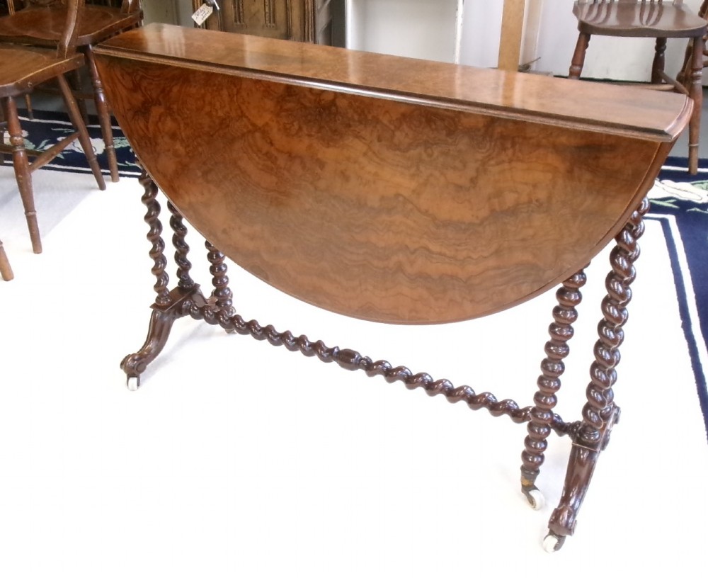A Victorian burr walnut Sutherland table featuring hinged drop leaves, spiralled barley twist legs, and white ceramic castors. View II