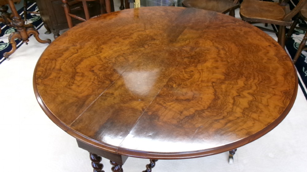 A Victorian burr walnut Sutherland table featuring hinged drop leaves, spiralled barley twist legs, and white ceramic castors. View III