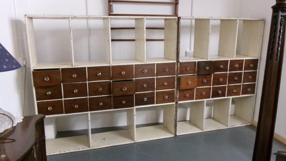 A pair of large Victorian painted shop fitting units featuring open cubby shelves and multiple dark wood drawers with round knobs.