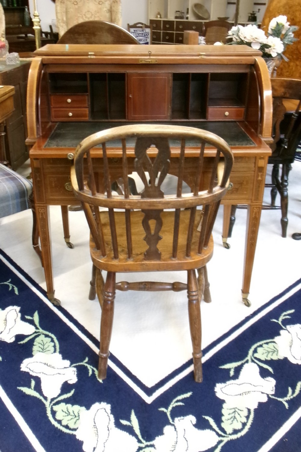 An antique Edwardian inlaid mahogany cylinder top writing desk featuring an open curved roll top, fitted internal compartments, a green leather writing surface, and tapered square legs with brass castors. View XII