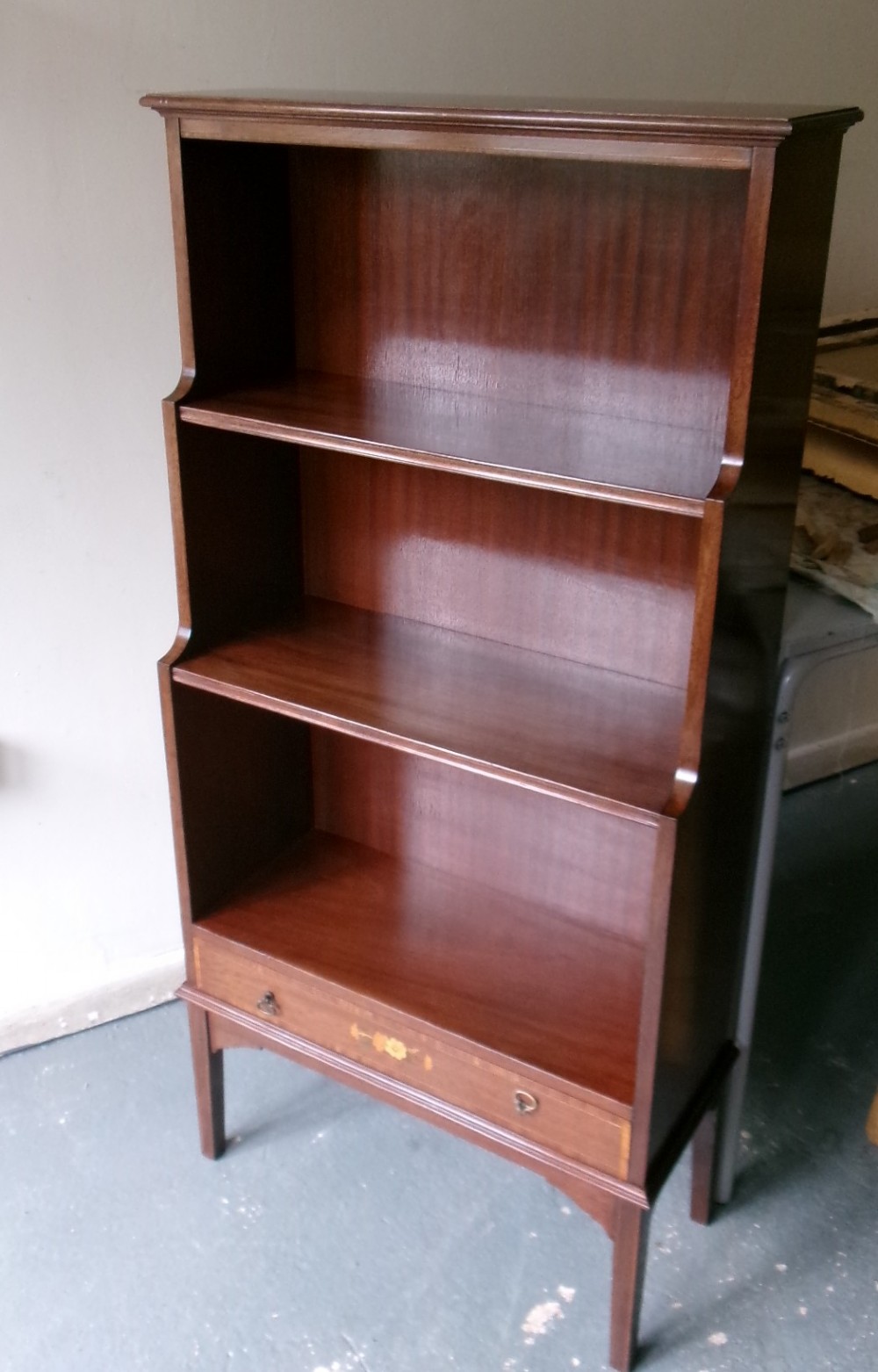 An Edwardian open mahogany bookcase featuring three shelves above a single drawer decorated with floral inlay. View V