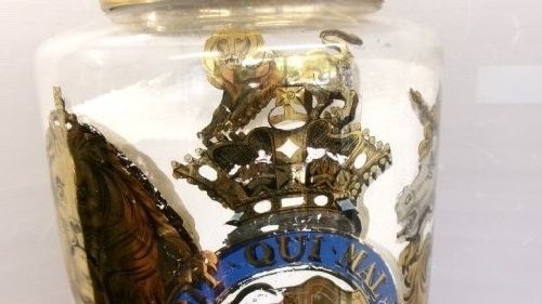 A large clear glass Victorian apothecary jar featuring a gilded coat of arms and arrowroot inscription topped with a fitted domed brass lid. View III