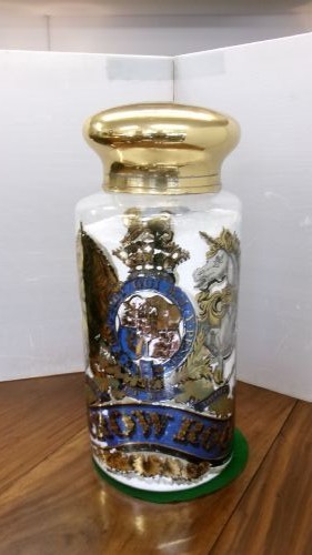 A large clear glass Victorian apothecary jar featuring a gilded coat of arms and arrowroot inscription topped with a fitted domed brass lid. View XI